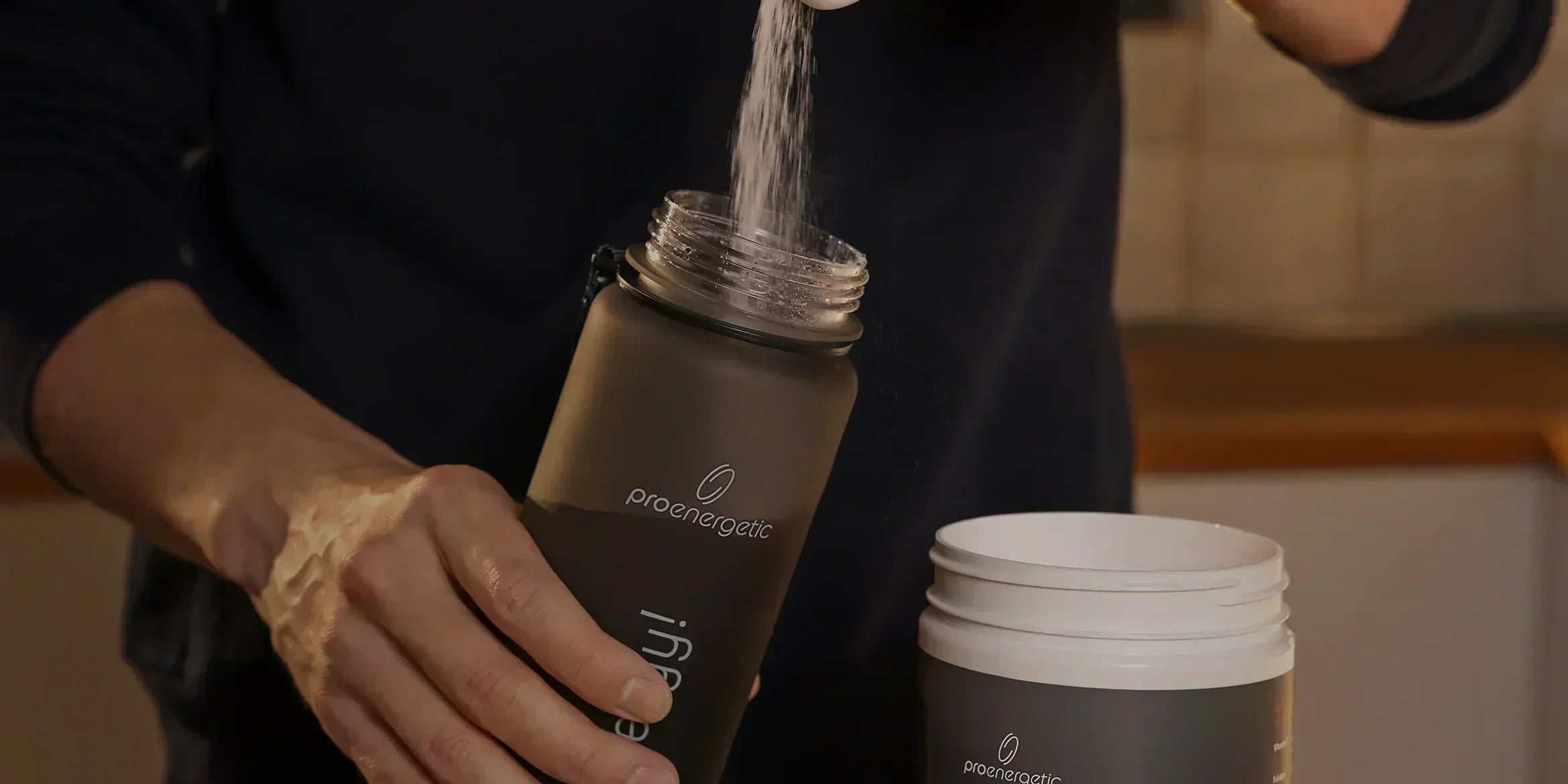 Person füllt Isomove isotonisches Pulver aus Messlöffel in schwarze Pure Move Trinkflasche neben geöffnetem Behälter