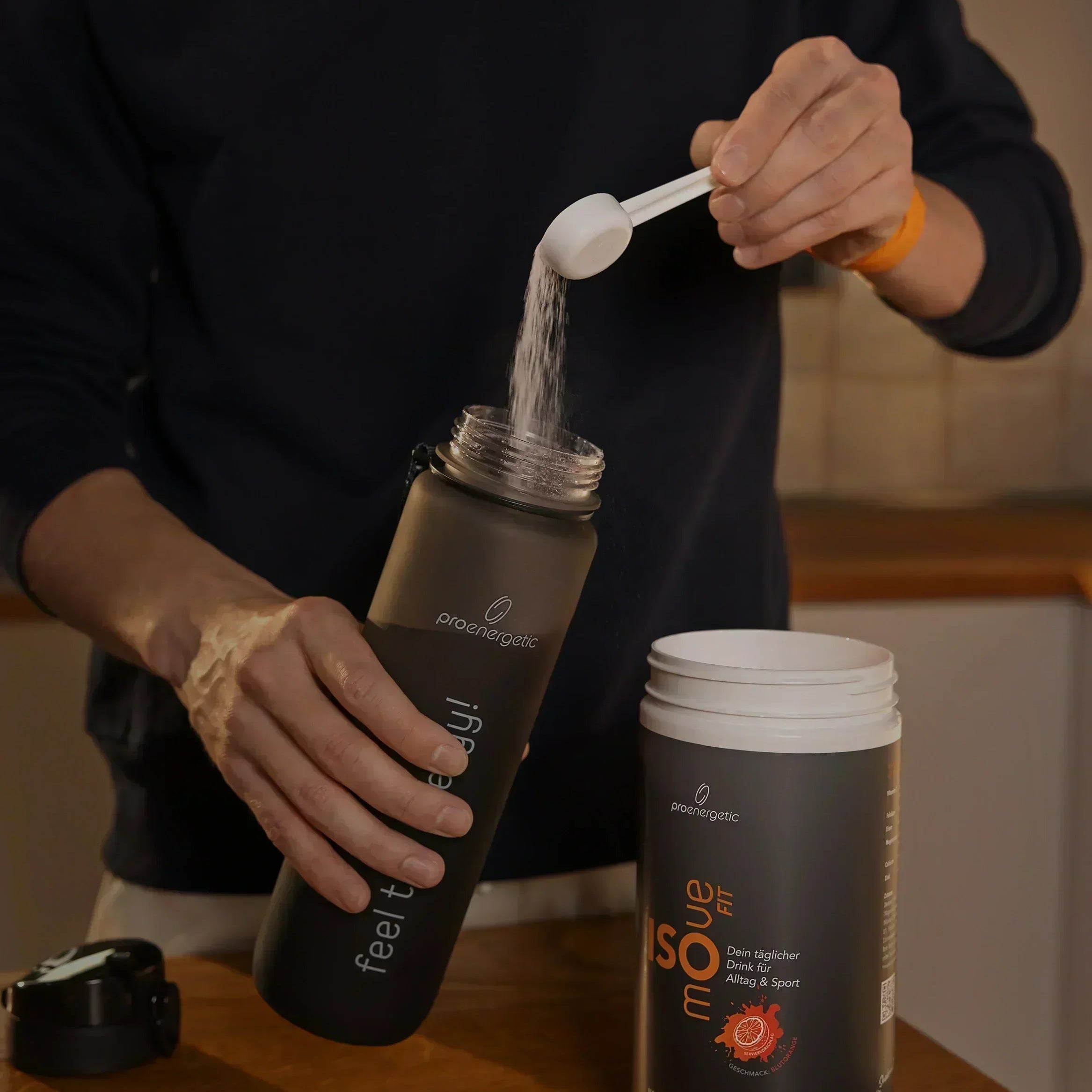 Person füllt Isomove isotonisches Pulver aus Messlöffel in schwarze Pure Move Trinkflasche neben geöffnetem Behälter