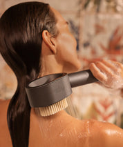 Person duscht von der Seite gesehen und hält den AERO Shower Duschkopf mit Bürsten-Aufsatz am Nacken, Wasser fließt über Haut und Haar