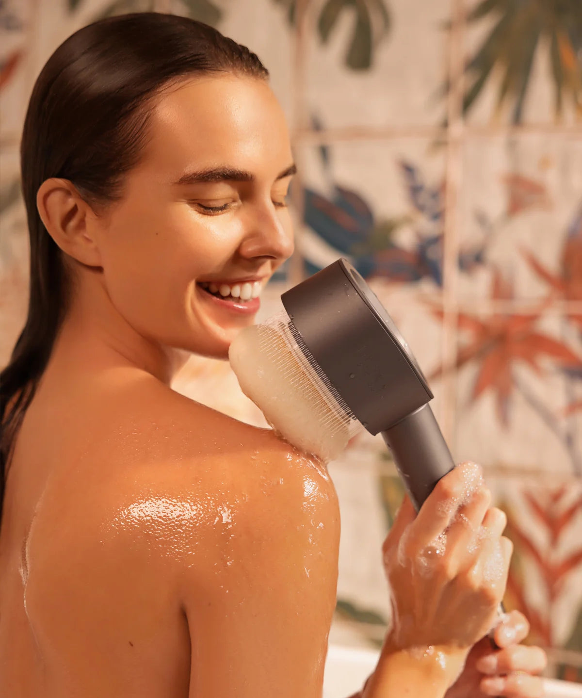 Person duscht im Badezimmer und hält den AERO Shower Duschkopf mit Peeling-Aufsatz an die Schulter, Haut ist nass und glänzend