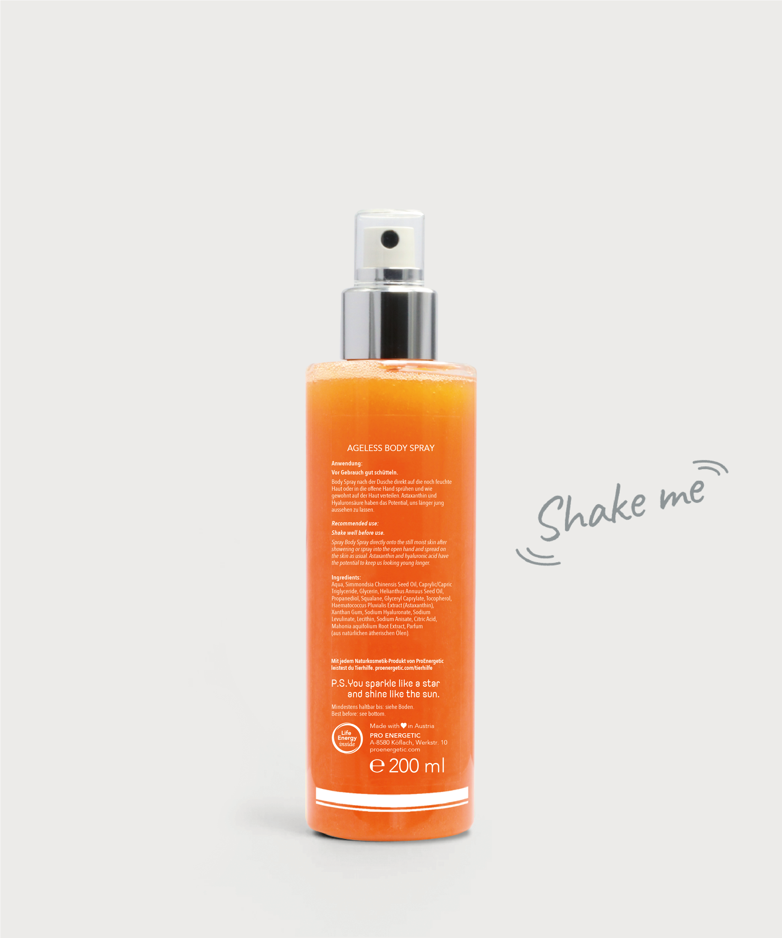 Ageless Body Spray von hinten: transparente Sprühflasche mit silbernem Pumpkopf, gefüllt mit orangefarbener Flüssigkeit, Rückseitenbeschriftung sichtbar, daneben der Hinweis „Shake me“, vor hellem Hintergrund.