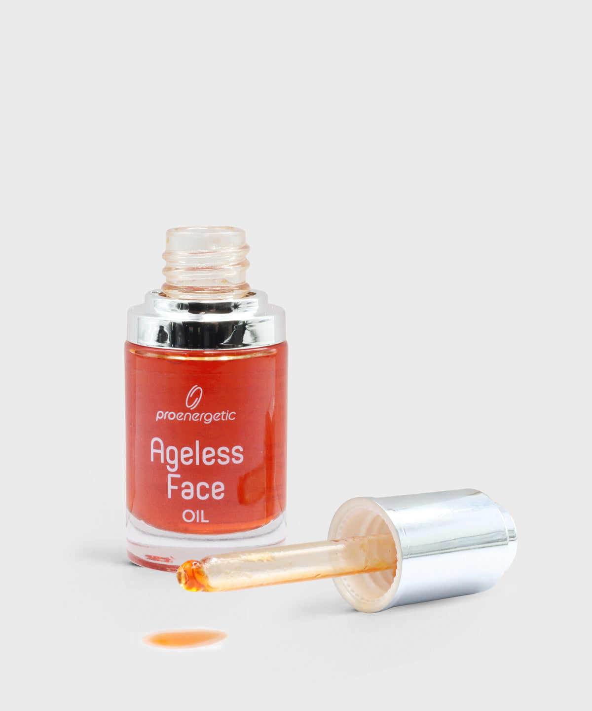 Offene Glasflasche „Ageless Face Oil“ mit silberner Pipette, orangefarbenes Gesichtsöl sichtbar, ein Tropfen Öl auf hellem, neutralem Untergrund.