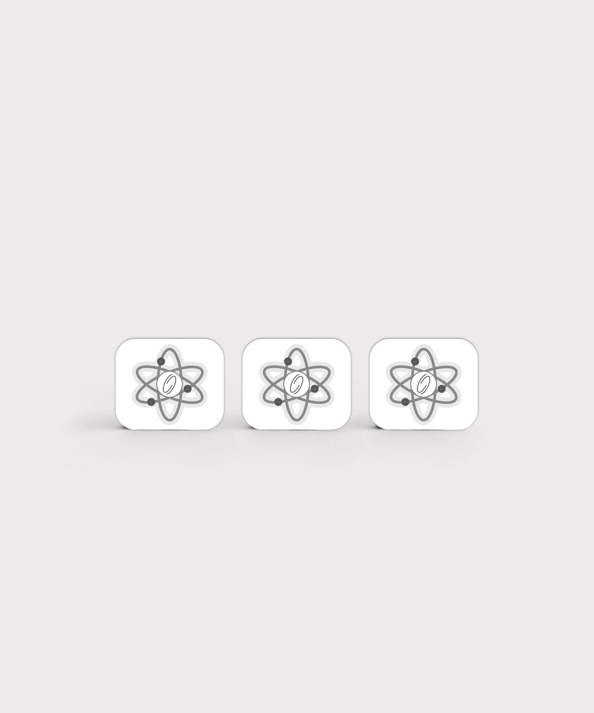 Drei weiße, quadratische Aufkleber mit abgerundeten Ecken liegen nebeneinander. Auf jedem Kleber ist ein graues, stilisiertes Atom-Symbol mit zentralem Punkt abgebildet. Minimalistisches Produktdesign auf hellem, neutralem Hintergrund.