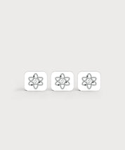 Drei weiße, quadratische Aufkleber mit abgerundeten Ecken liegen nebeneinander. Auf jedem Kleber ist ein graues, stilisiertes Atom-Symbol mit zentralem Punkt abgebildet. Minimalistisches Produktdesign auf hellem, neutralem Hintergrund.