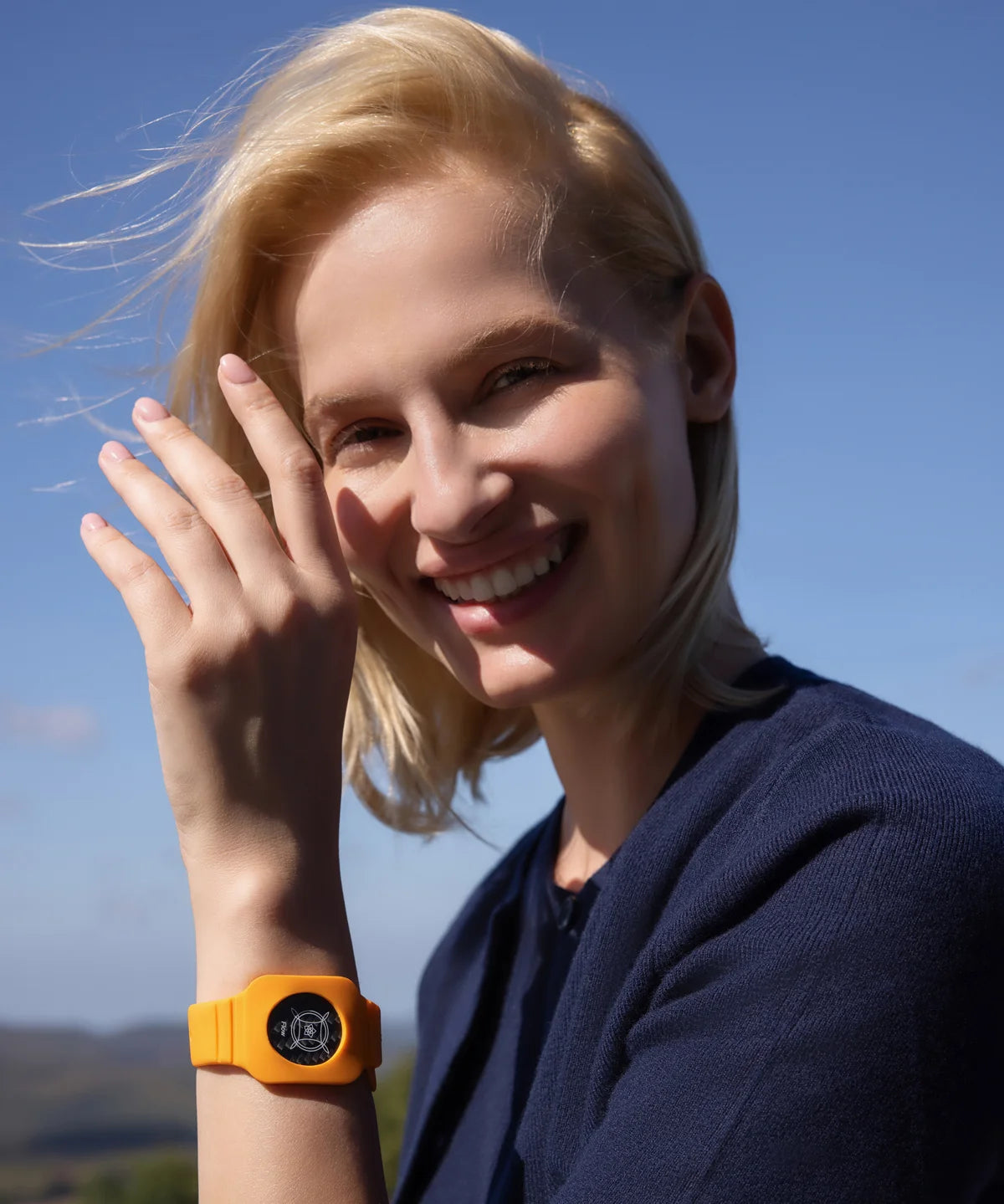 Lächelnde Person im Freien mit blonden Haaren, die ein oranges Eloop Band mit eingesetztem Eloop Chip Flow am Handgelenk trägt.