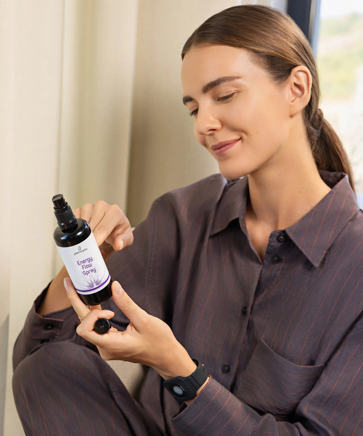Person sitzt im Innenraum und hält das Energy Flow Spray in schwarzer Sprühflasche, betrachtet das Etikett bei natürlichem Licht