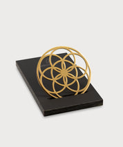 Flower of Love Goodie als goldenes Ornament in geometrischer Blütenform auf schwarzem Sockel vor hellem Hintergrund