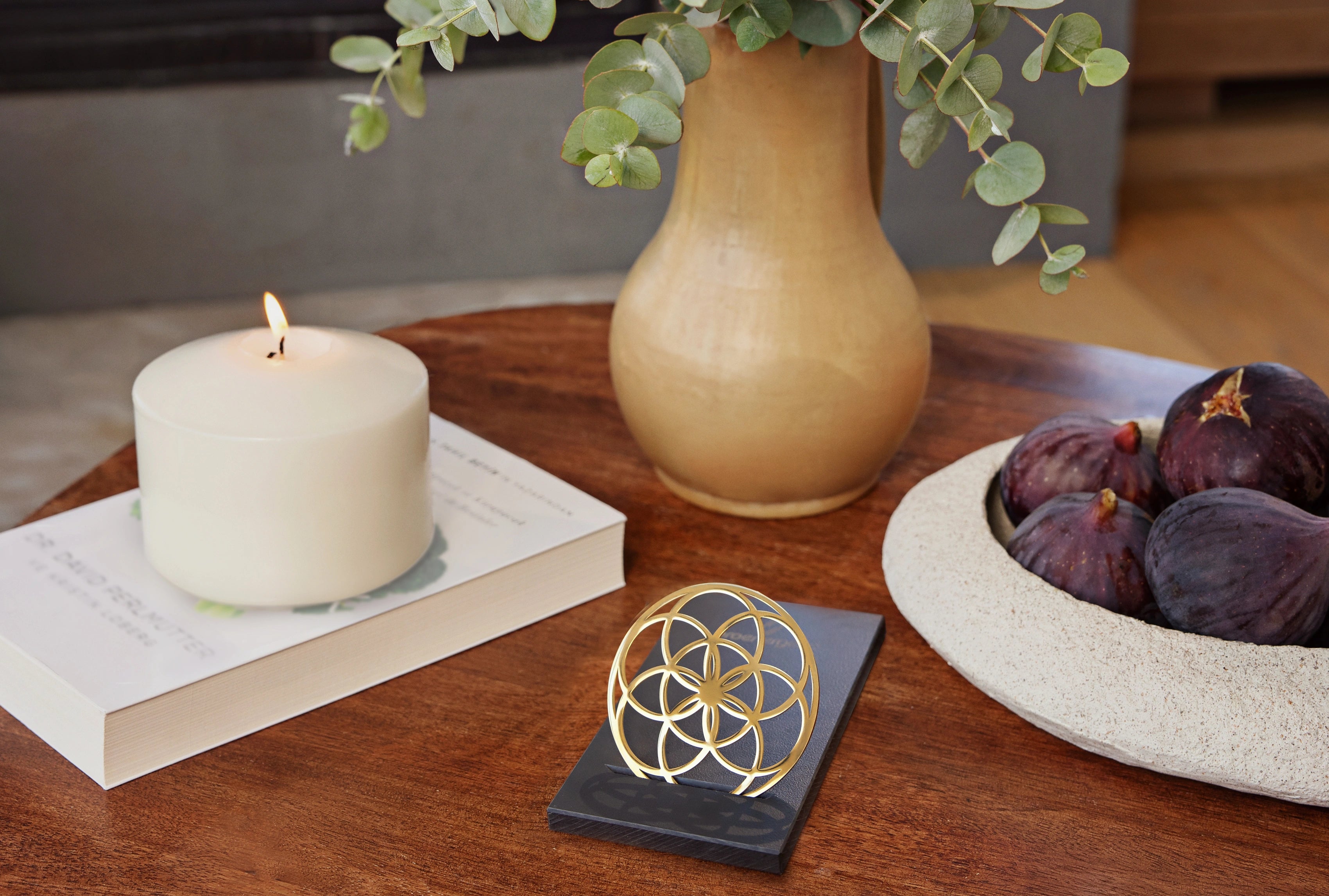 Flower of Love Goodie als goldenes Ornament auf schwarzem Sockel, arrangiert auf einem Holztisch in wohnlicher Umgebung