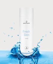Fresh Skin Tonic von proenergetic: weiße, zylindrische Flasche mit hellblauer Beschriftung steht in spritzendem Wasser, frischer Clean-Beauty-Look, symbolisiert Feuchtigkeit und Erfrischung, neutraler Hintergrund.