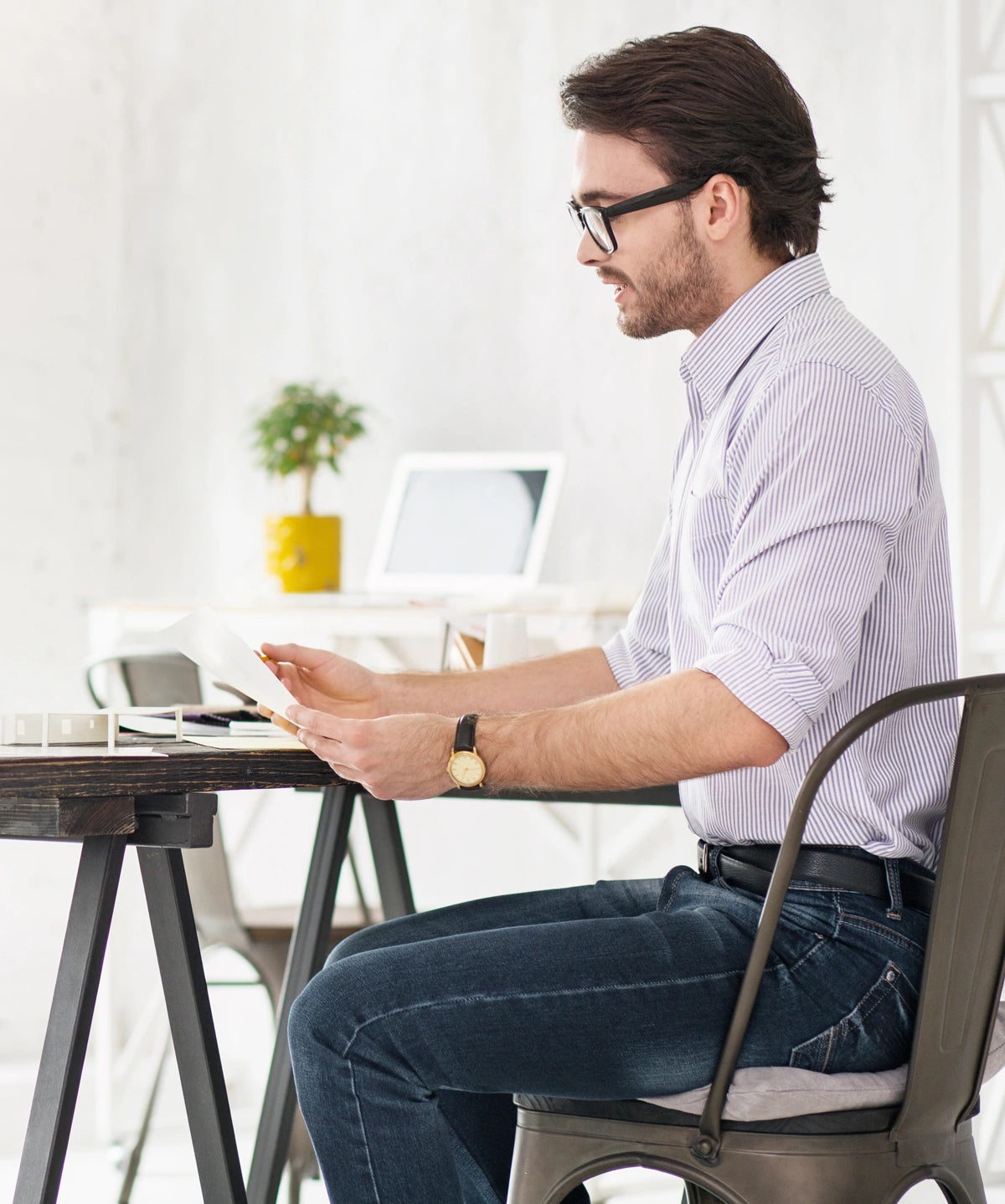 Person sitzt an einem Schreibtisch am Fenster und arbeitet am Laptop, auf dem Stuhl liegt ein weißes Grounding Relax Pad