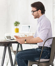 Person sitzt an einem Schreibtisch am Fenster und arbeitet am Laptop, auf dem Stuhl liegt ein weißes Grounding Relax Pad