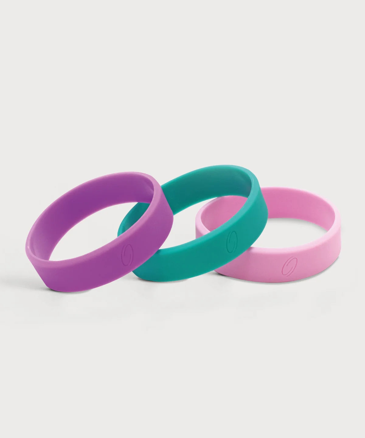 Drei ProEnergetic Kids Band Armbänder aus Silikon in Lila, Türkis und Rosa mit glatter Oberfläche und dezent eingeprägtem Markenlogo auf hellem Hintergrund