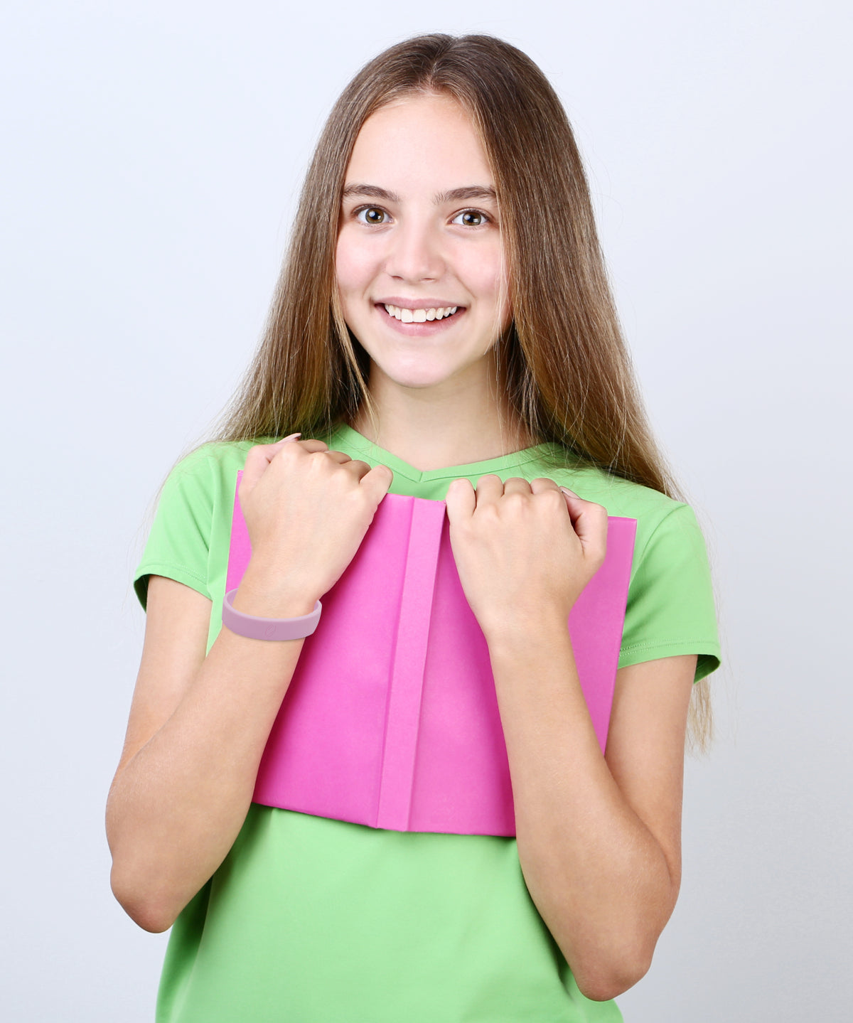 Mädchen steht im Innenraum und hält ein pinkes Heft, am Handgelenk trägt sie ein rosa ProEnergetic Kids Band aus Silikon