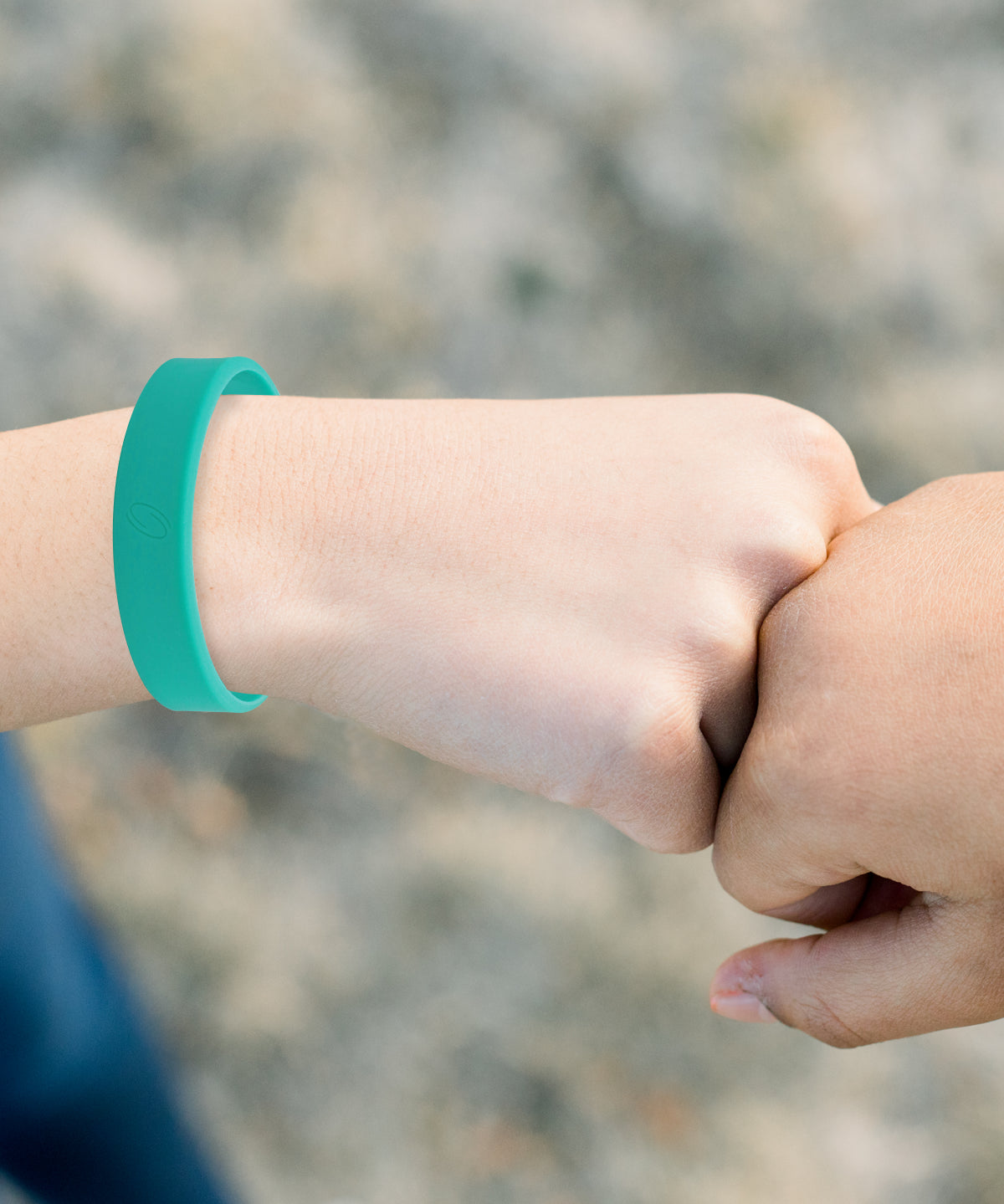 Kinderhand mit getragenem türkisem ProEnergetic Kids Band aus Silikon am Handgelenk, zweite Hand im Vordergrund bei Faustberührung sichtbar