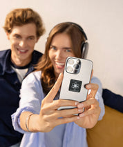 Zwei Personen sitzen im Innenraum, eine Frau hält ein Smartphone mit angebrachtem KIER Protect Mobile Element in die Kamera