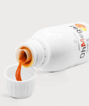 Geöffnete Flasche „OhMega! Omega 3 Liquid“ von proenergetic, aus der orangefarbene Flüssigkeit in den weißen Messdeckel gegossen wird, Nahaufnahme auf hellem Studiohintergrund.