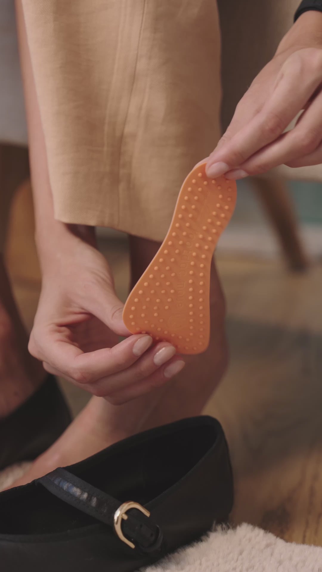 Hände setzen eine orangefarbene Footdoc Insoles MOVE | BALANCE-Einlegesohle in einen schwarzen Ballerina-Schuh ein; Nahaufnahme während der Anwendung, Videoaufnahme.