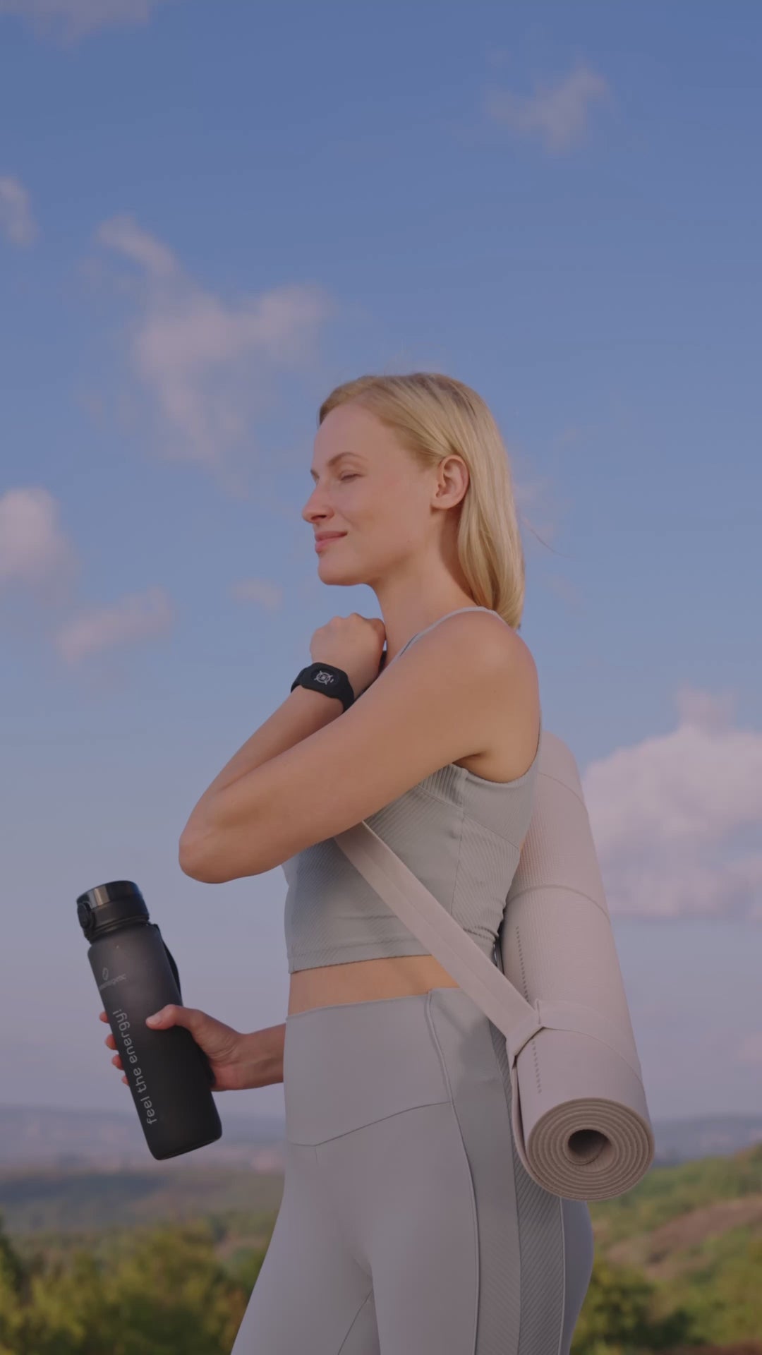 Person bewegt sich im Freien, trägt Eloop Band mit Chip und trinkt aus der schwarzen Pure Move Trinkflasche vor blauem Himmel