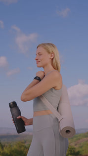 Person bewegt sich im Freien, trägt Eloop Band mit Chip und trinkt aus der schwarzen Pure Move Trinkflasche vor blauem Himmel