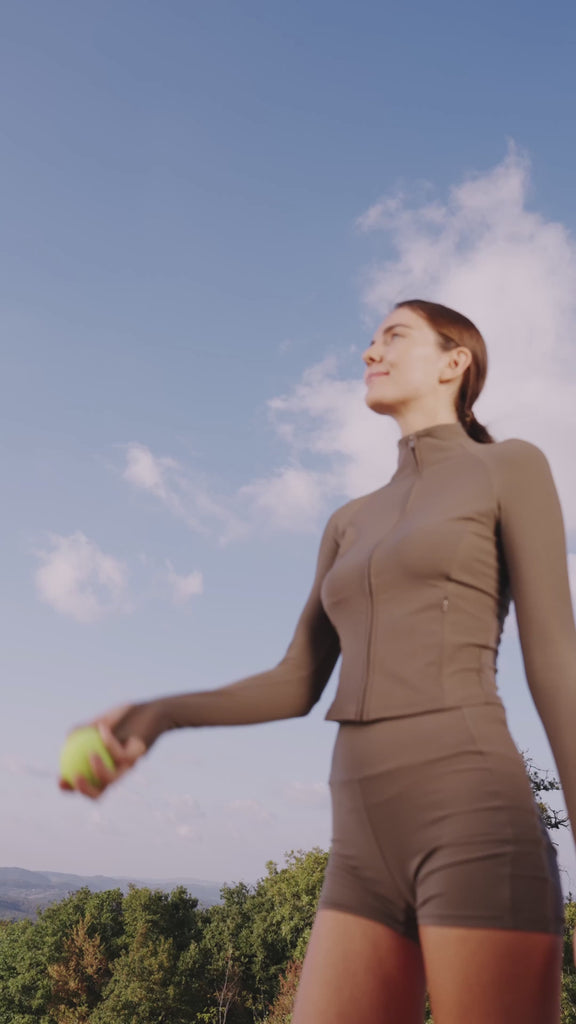 Person steht im Freien in Sportkleidung, spielt mit einem Tennisball und trägt ein oranges Eloop Band Silikonarmband am Handgelenk