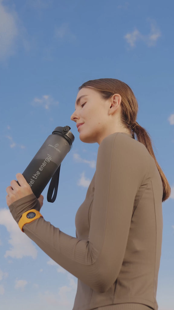 Person steht im Freien in Sportbekleidung und hält die schwarze Pure Move Trinkflasche mit ausgestrecktem Arm vor blauem Himmel