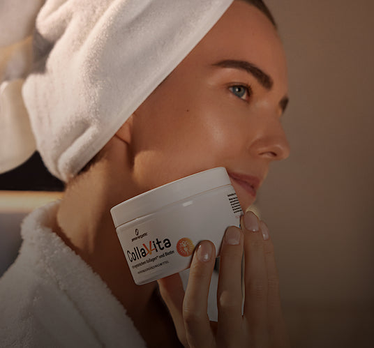 Frau mit weißem Handtuch auf dem Kopf hält Kollagen-Supplement-Glas nah an ihrem Gesicht